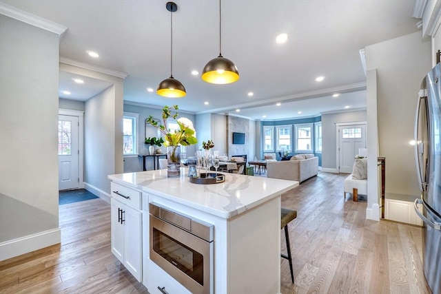 kitchen featuring stainless steel refrigerator, built in microwave, white cabinetry, hanging light fixtures, and ornamental molding