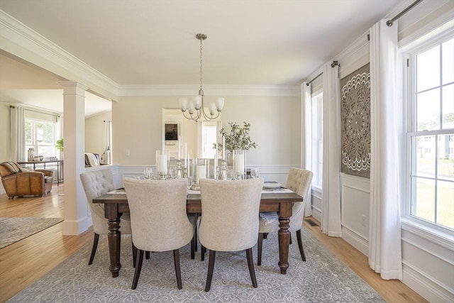 dining room featuring a notable chandelier, light hardwood / wood-style floors, ornamental molding, and decorative columns