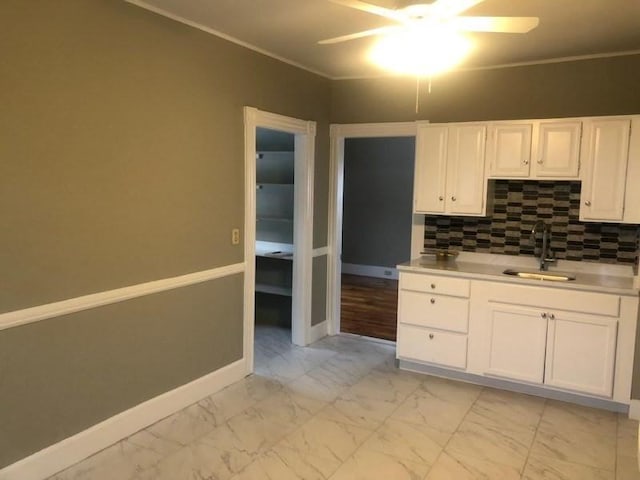 kitchen featuring marble finish floor, light countertops, backsplash, white cabinetry, and a sink