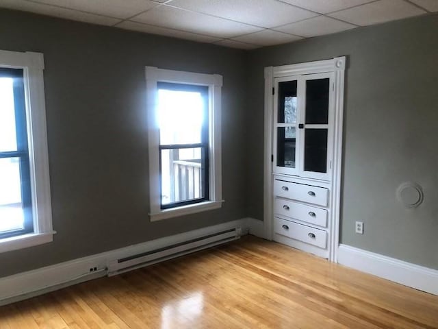 interior space featuring light wood-style floors, baseboard heating, a drop ceiling, and baseboards