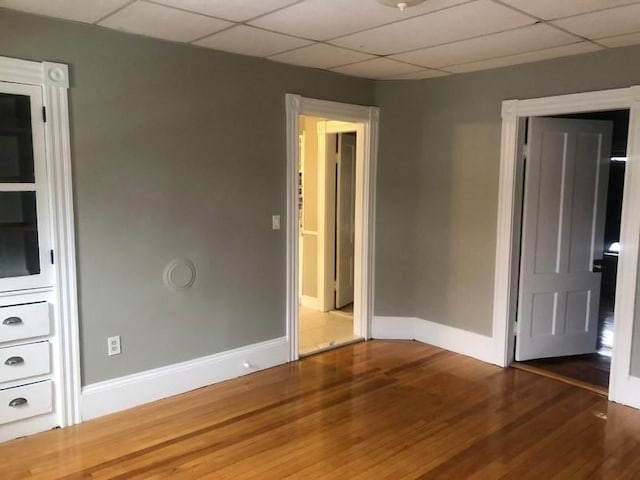 empty room with wood finished floors, a paneled ceiling, and baseboards