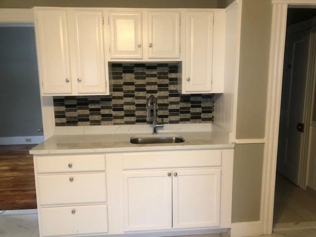 kitchen with white cabinets, light countertops, a sink, and decorative backsplash