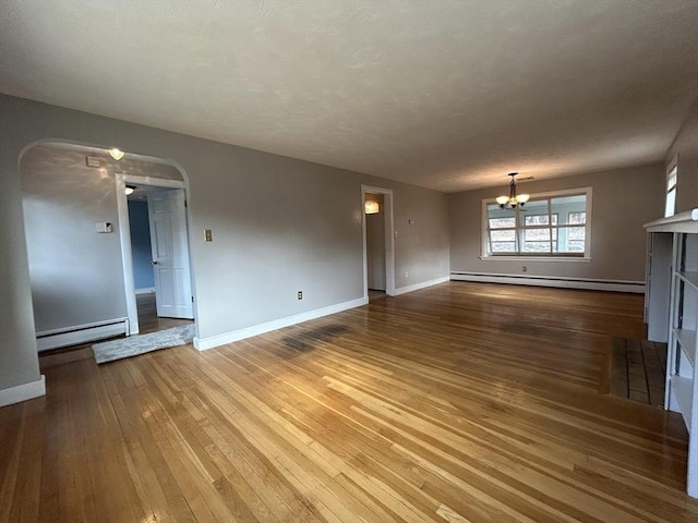 unfurnished living room with a baseboard heating unit, arched walkways, an inviting chandelier, and hardwood / wood-style floors