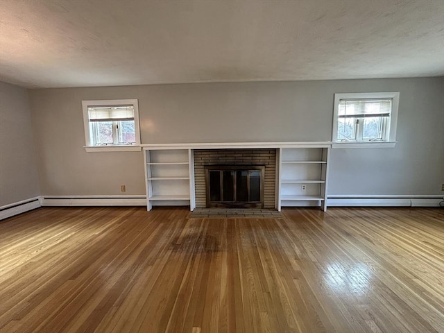 unfurnished living room with baseboard heating, hardwood / wood-style floors, a fireplace, and a textured ceiling