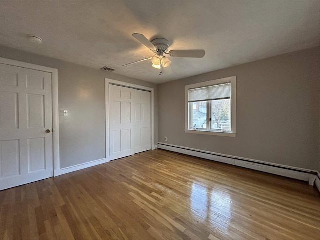 unfurnished bedroom featuring visible vents, a baseboard heating unit, wood finished floors, a closet, and baseboards