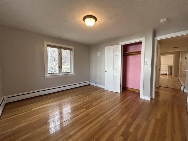 unfurnished bedroom with baseboards, baseboard heating, a closet, a textured ceiling, and dark wood-style flooring