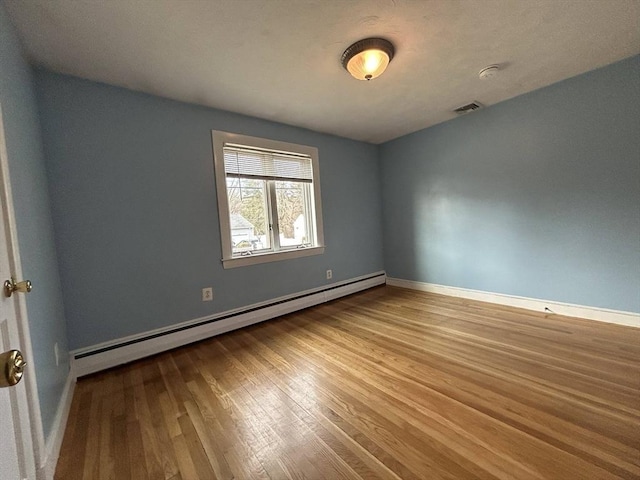 spare room with visible vents, a baseboard heating unit, baseboards, and wood finished floors