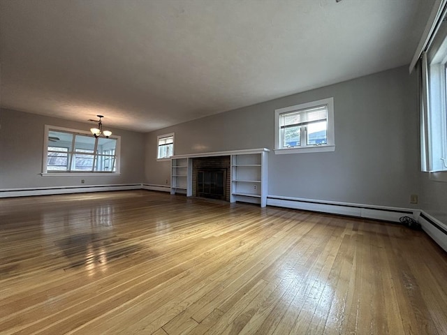 unfurnished living room featuring a chandelier, plenty of natural light, a baseboard heating unit, and wood-type flooring