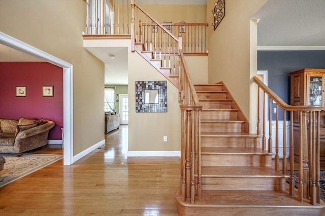 stairs featuring ornamental molding, a high ceiling, baseboards, and wood finished floors