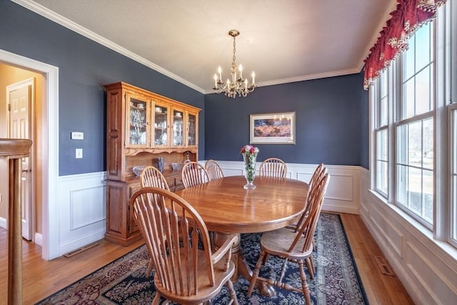 dining area with a wainscoted wall, an inviting chandelier, light wood-style floors, and ornamental molding