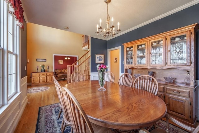 dining space with an inviting chandelier, stairway, light wood-style flooring, and crown molding