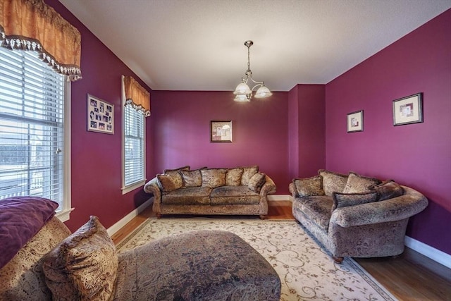 living area featuring an accent wall, wood finished floors, baseboards, and a chandelier