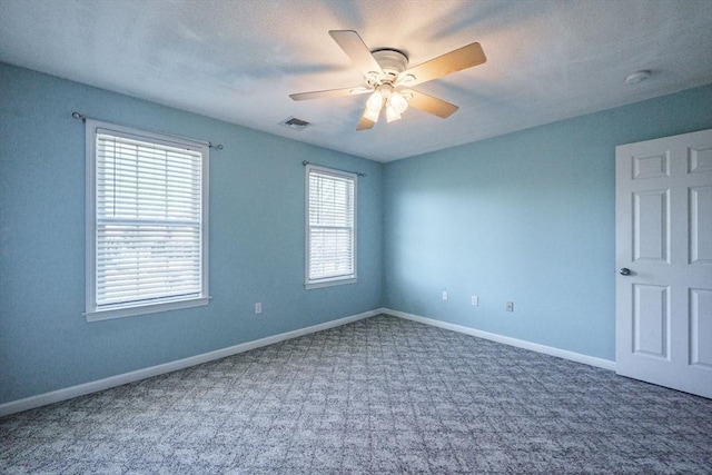 carpeted empty room featuring visible vents, a ceiling fan, and baseboards