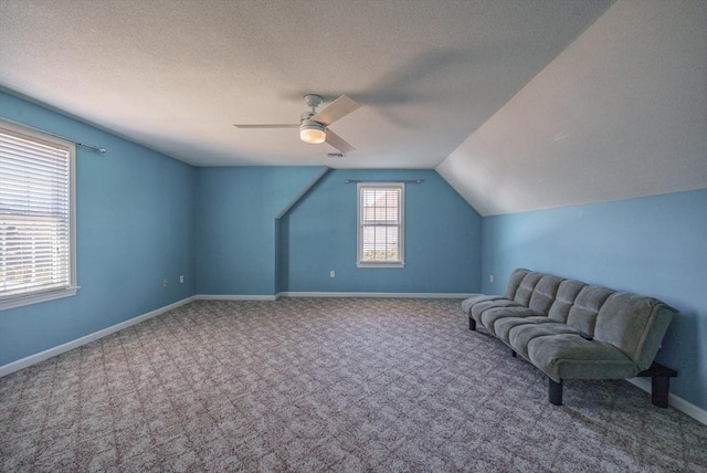 interior space featuring lofted ceiling, a ceiling fan, a textured ceiling, carpet flooring, and baseboards