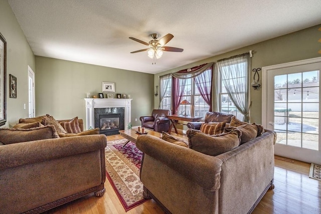 living room with ceiling fan, a textured ceiling, wood finished floors, and a premium fireplace