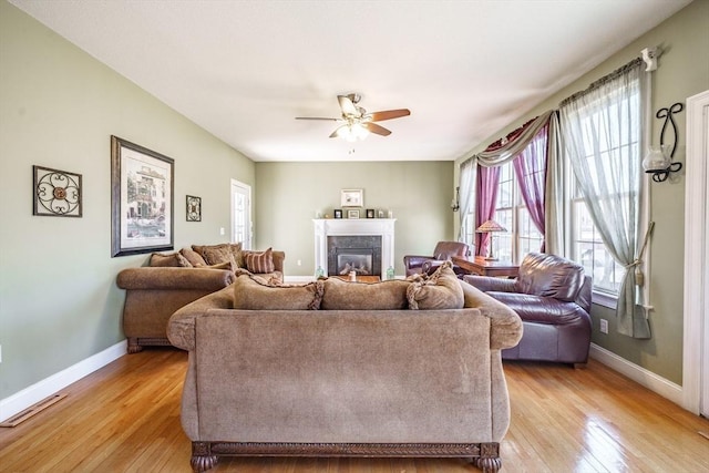 living area with light wood finished floors, visible vents, baseboards, a premium fireplace, and a ceiling fan