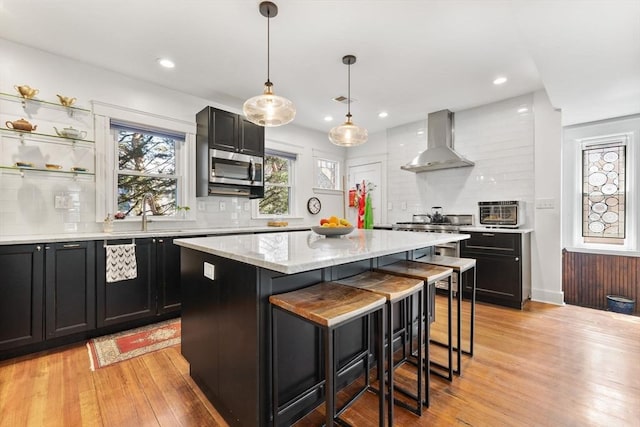 kitchen featuring wall chimney range hood, dark cabinetry, and a sink