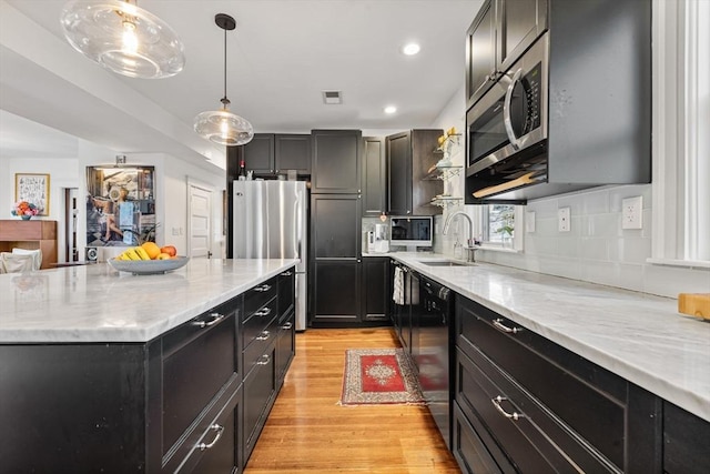 kitchen featuring visible vents, light wood-type flooring, a sink, dark cabinets, and stainless steel appliances