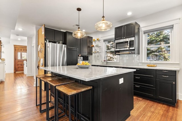 kitchen with dark cabinets, stainless steel microwave, light wood finished floors, and a center island