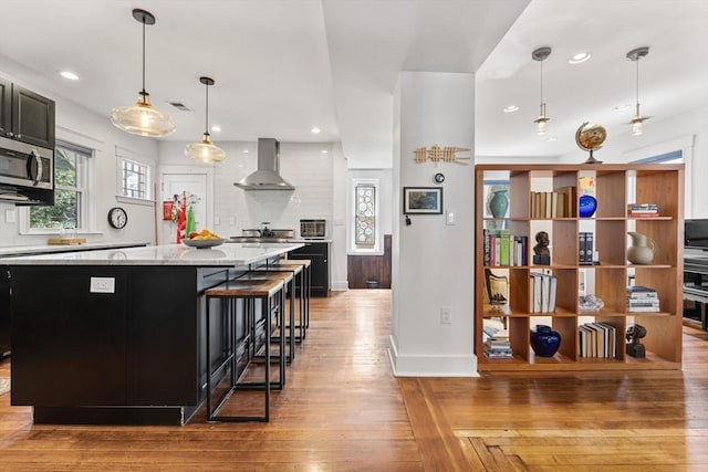 kitchen with stainless steel microwave, recessed lighting, and wall chimney exhaust hood