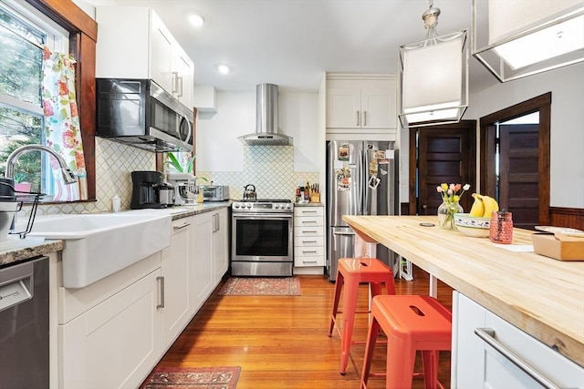 kitchen featuring butcher block countertops, a sink, appliances with stainless steel finishes, and wall chimney range hood