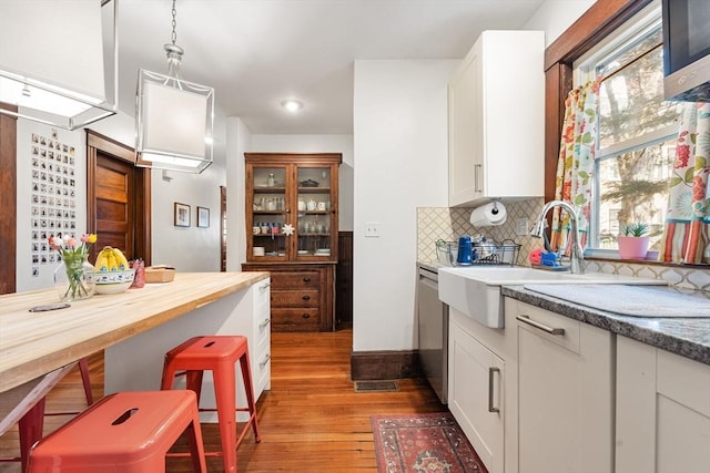 kitchen featuring white cabinetry, tasteful backsplash, a sink, light wood finished floors, and dishwasher
