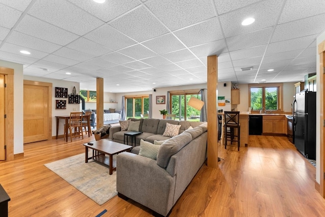 living room with light wood-type flooring, a paneled ceiling, and sink