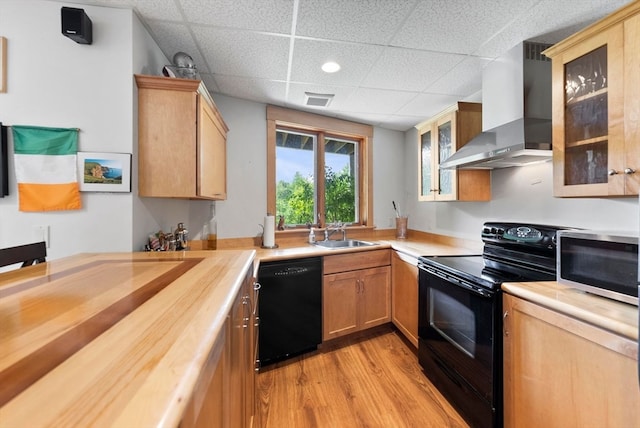 kitchen featuring wall chimney exhaust hood, black appliances, a drop ceiling, light hardwood / wood-style flooring, and sink