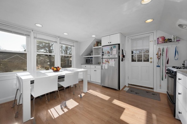 kitchen with light hardwood / wood-style flooring, stainless steel appliances, white cabinets, and vaulted ceiling