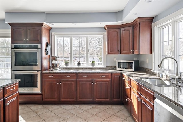 kitchen with dark stone counters, appliances with stainless steel finishes, a sink, and a wealth of natural light