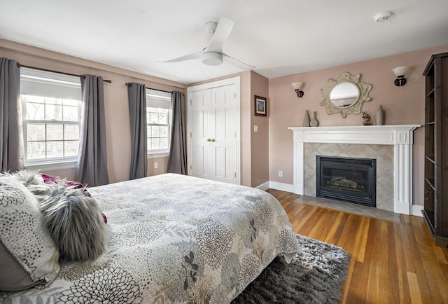 bedroom featuring ceiling fan, a fireplace, wood finished floors, baseboards, and a closet