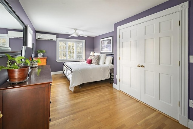 bedroom featuring baseboards, ceiling fan, a wall mounted air conditioner, and light wood-style floors