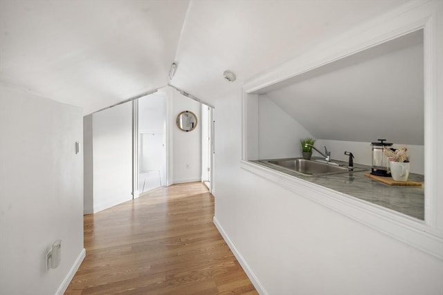 hallway featuring lofted ceiling, a sink, light wood-style flooring, and baseboards