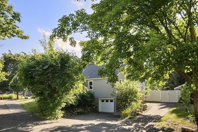 view of property exterior featuring driveway, an attached garage, and fence