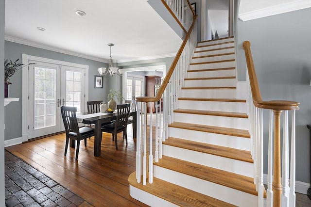 stairway with baseboards, wood-type flooring, crown molding, french doors, and a chandelier