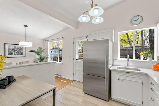 kitchen with stainless steel refrigerator, lofted ceiling with beams, light countertops, white cabinetry, and a sink