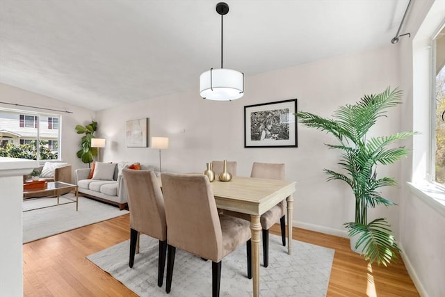 dining space with baseboards, vaulted ceiling, and light wood-type flooring