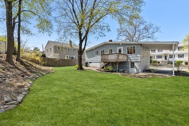 back of property with fence, a wooden deck, a yard, and an attached carport