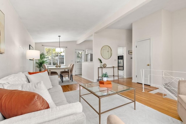living area featuring baseboards, vaulted ceiling with beams, and light wood finished floors