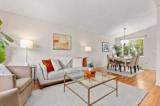 living area with baseboards, vaulted ceiling, and light wood-type flooring