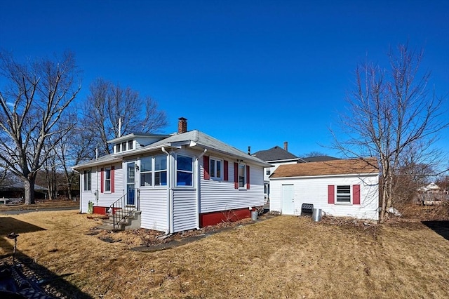 view of side of home with entry steps, an outdoor structure, a yard, and a chimney