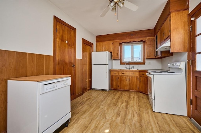 kitchen featuring white appliances, brown cabinetry, a sink, under cabinet range hood, and wainscoting