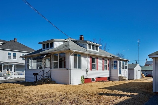 view of front of property featuring entry steps, a detached garage, a sunroom, and a chimney