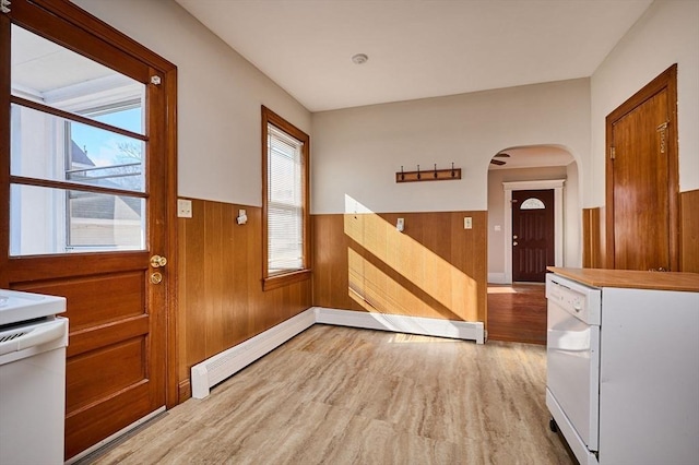 interior space with baseboard heating, wainscoting, light wood-style flooring, and wooden walls