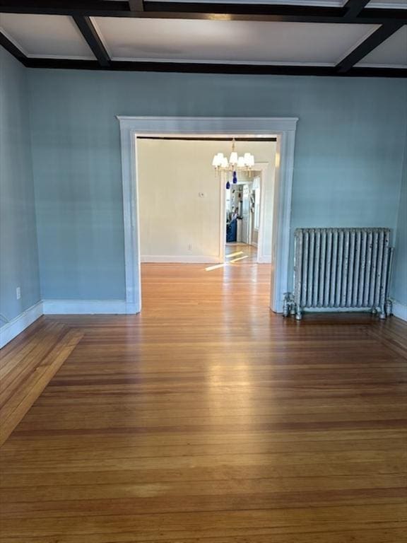 empty room featuring hardwood / wood-style floors, coffered ceiling, radiator, and a chandelier