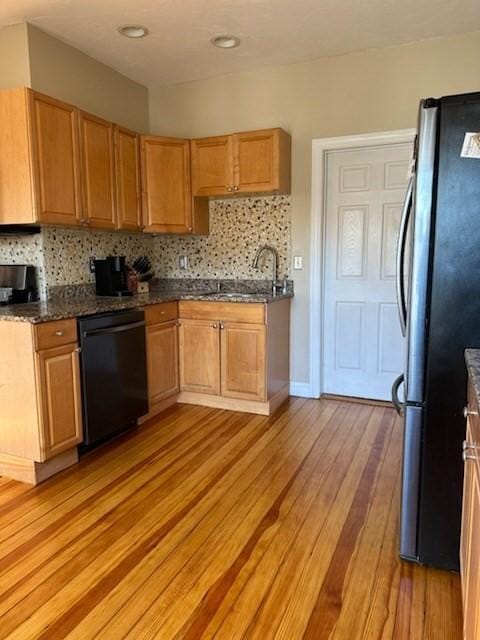 kitchen with decorative backsplash, sink, black dishwasher, light hardwood / wood-style floors, and stainless steel refrigerator