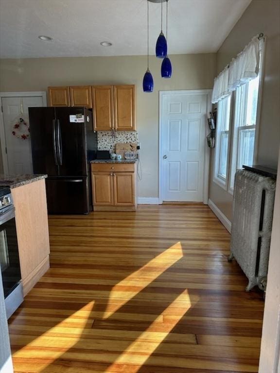 kitchen featuring radiator heating unit, stainless steel range oven, dark hardwood / wood-style floors, decorative light fixtures, and black refrigerator