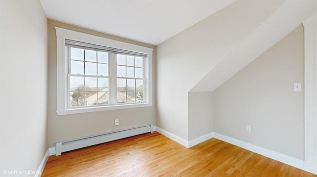 additional living space with lofted ceiling, a baseboard heating unit, and light hardwood / wood-style floors