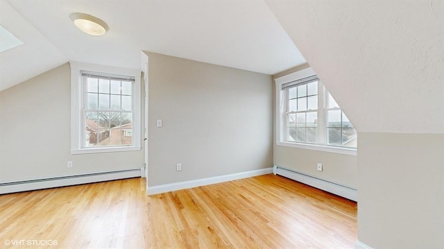 additional living space with hardwood / wood-style floors, a baseboard radiator, vaulted ceiling, and plenty of natural light