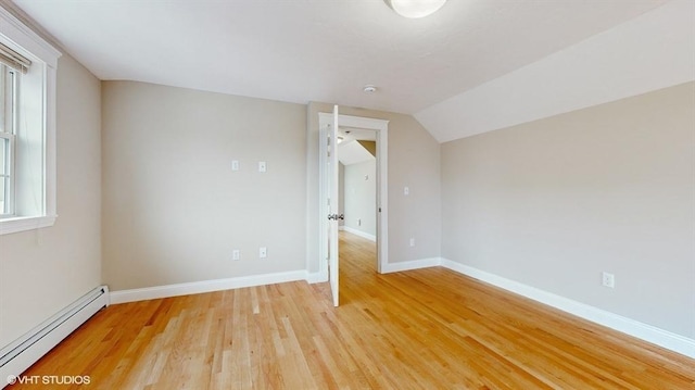 additional living space with a baseboard heating unit, vaulted ceiling, and light hardwood / wood-style floors